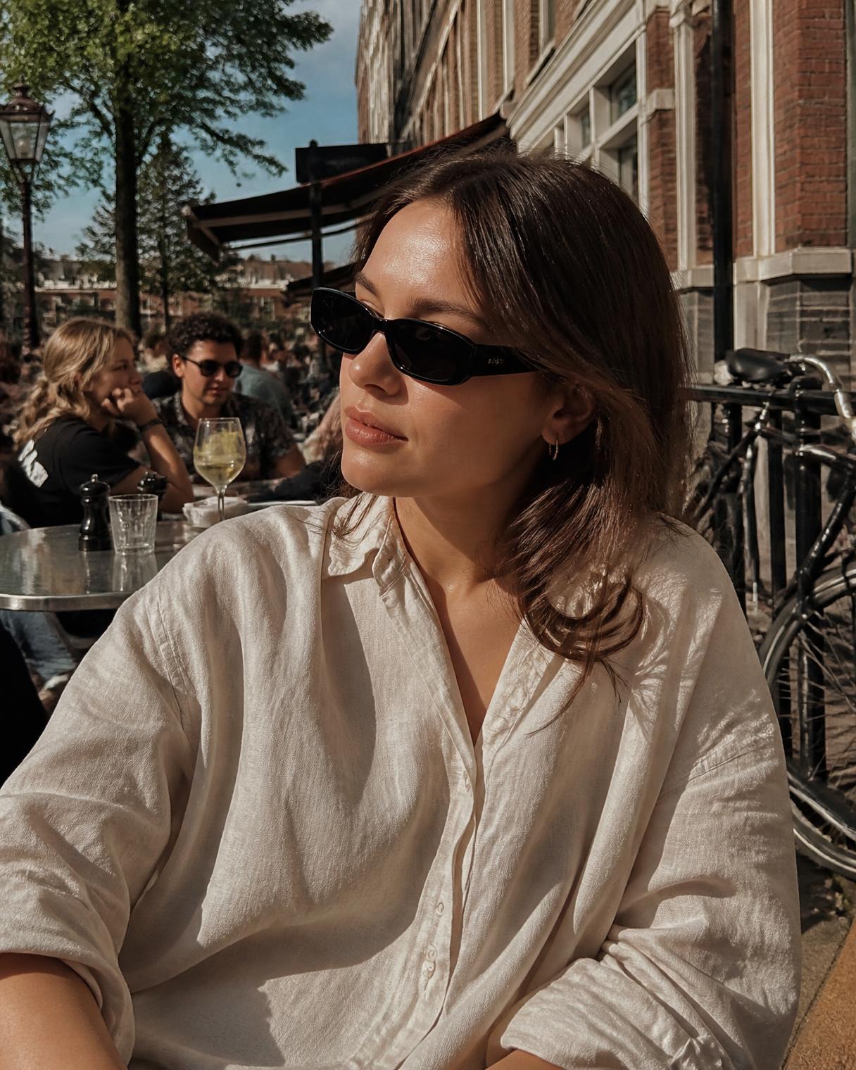 Vrouw met zonnebril op een zonnig terras in De Pijp in Amsterdam