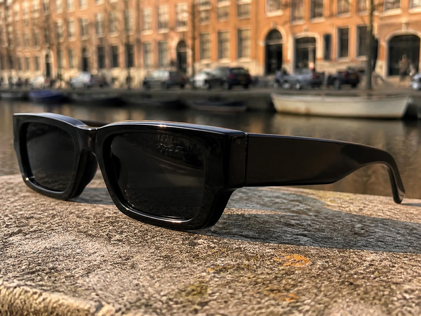 Detailopname van een rechthoekige zonnebril op een stenen kade langs de gracht